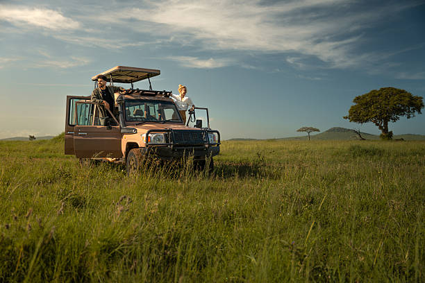 Man and woman standing on the side steps of an open safari vehicle in Serengeti National Park, experiencing Tanzania Budget vs Luxury Safaris in the vast green grasslands of Tanzania
